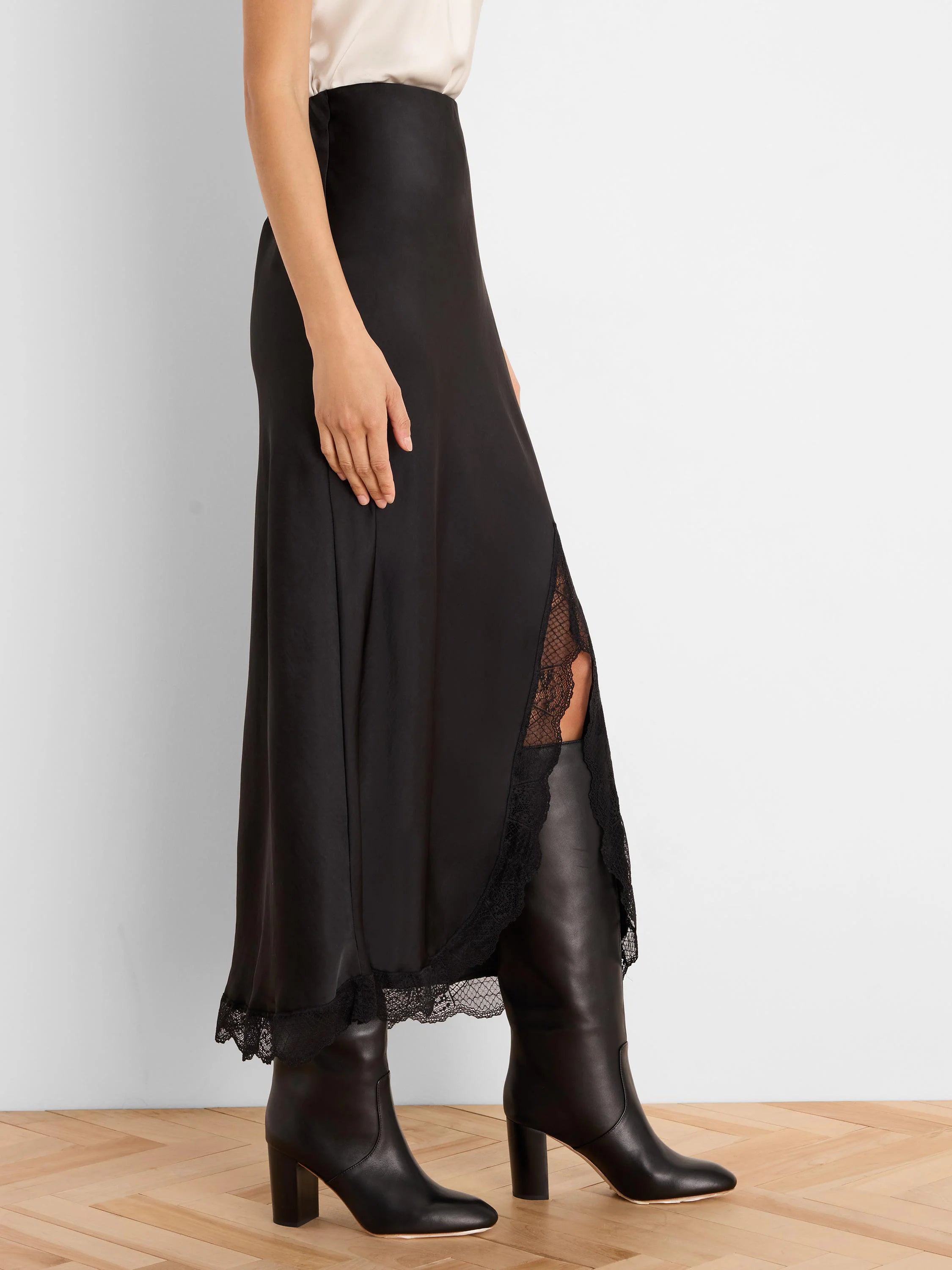Black glossy midi slip skirt with black lace trim at the hem and a deep side slit revealing lace fabric.