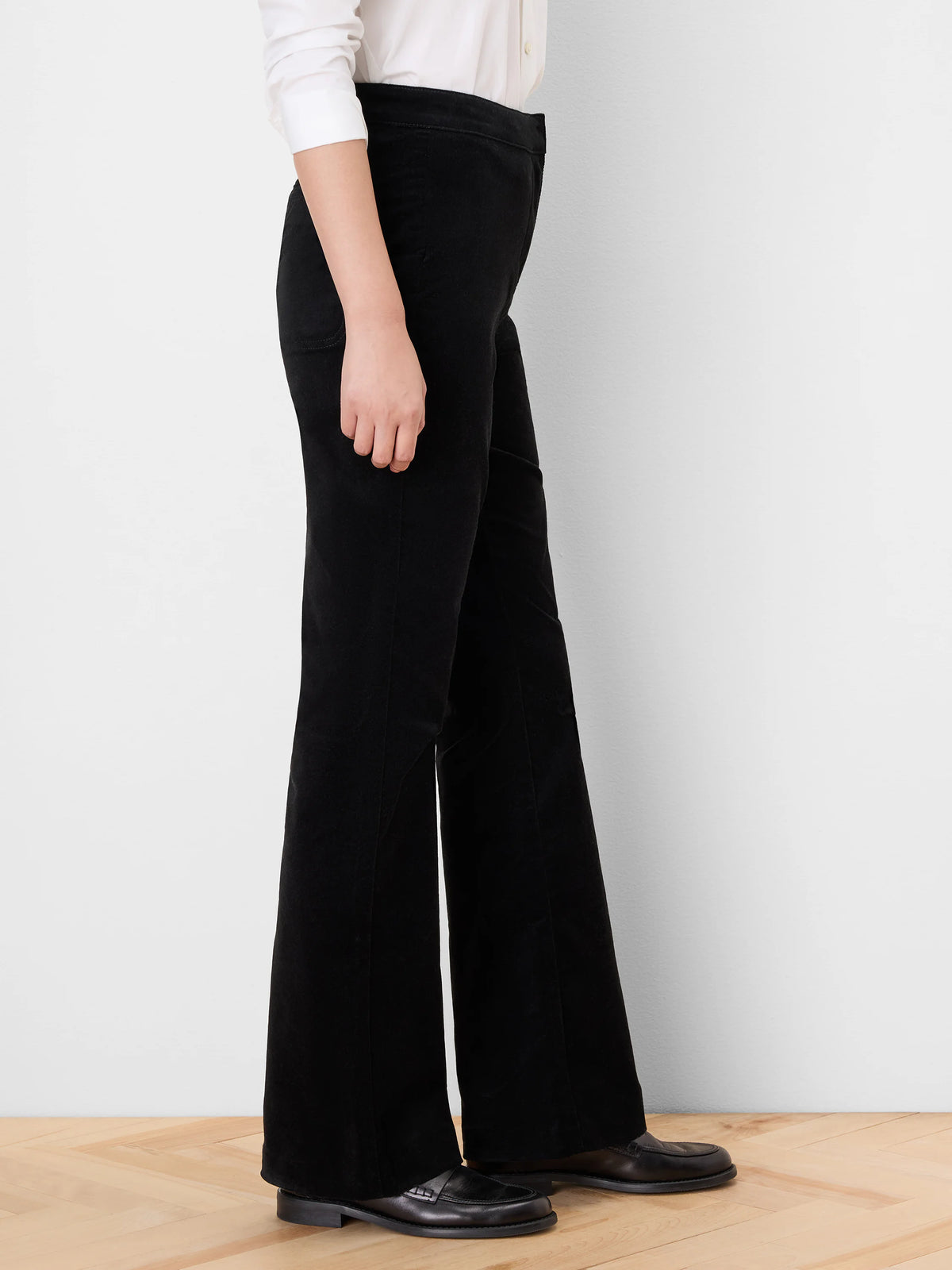 Black velvet high-rise boot-cut pants, side view. Legs flare widely from the knee, covering the feet.
