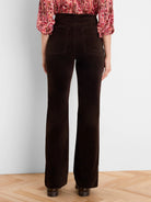 Dark brown velvet boot-cut pants on model from behind. Features back patch pockets and a subtle leg flare.