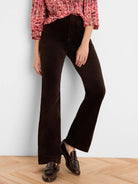 Dark brown high-rise velvet bootcut pants on a model. Fabric has a soft, plush texture and subtle sheen.