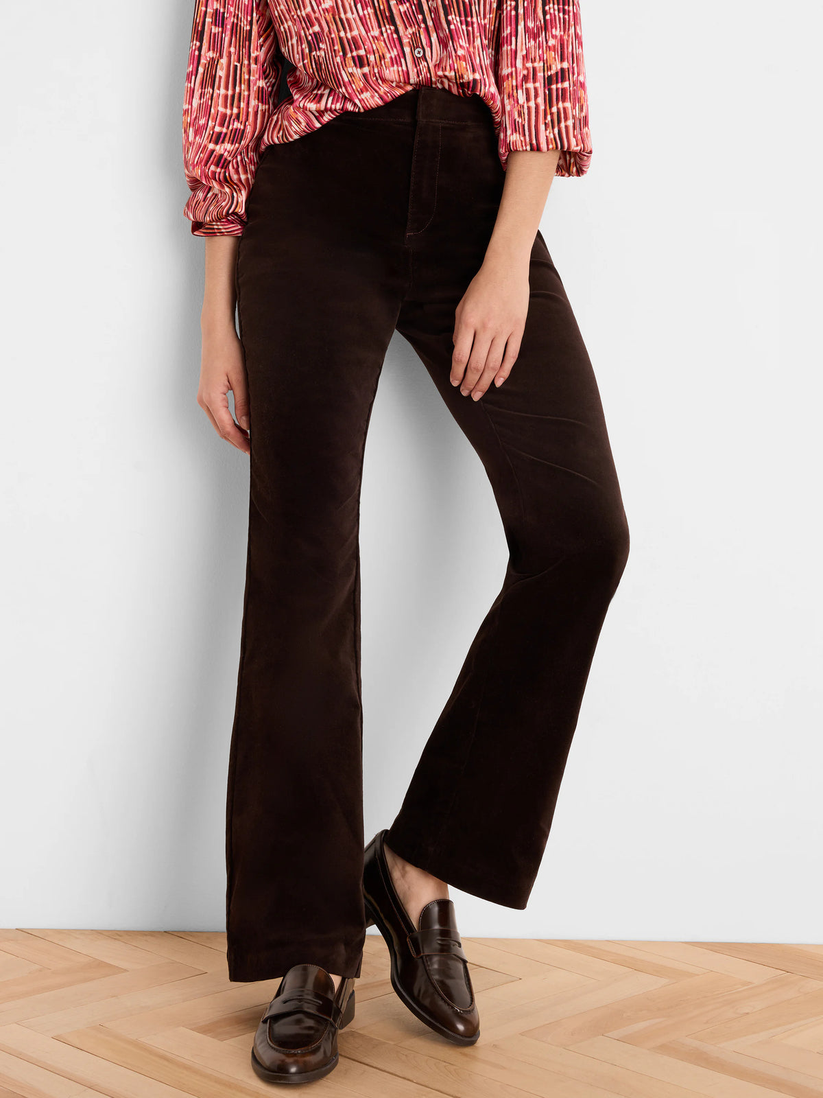Dark brown high-rise velvet bootcut pants on a model. Fabric has a soft, plush texture and subtle sheen.