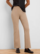 Tan, high-waisted bootcut pants on a person. Slim-fit through legs, subtle flare at hem. Smooth fabric.