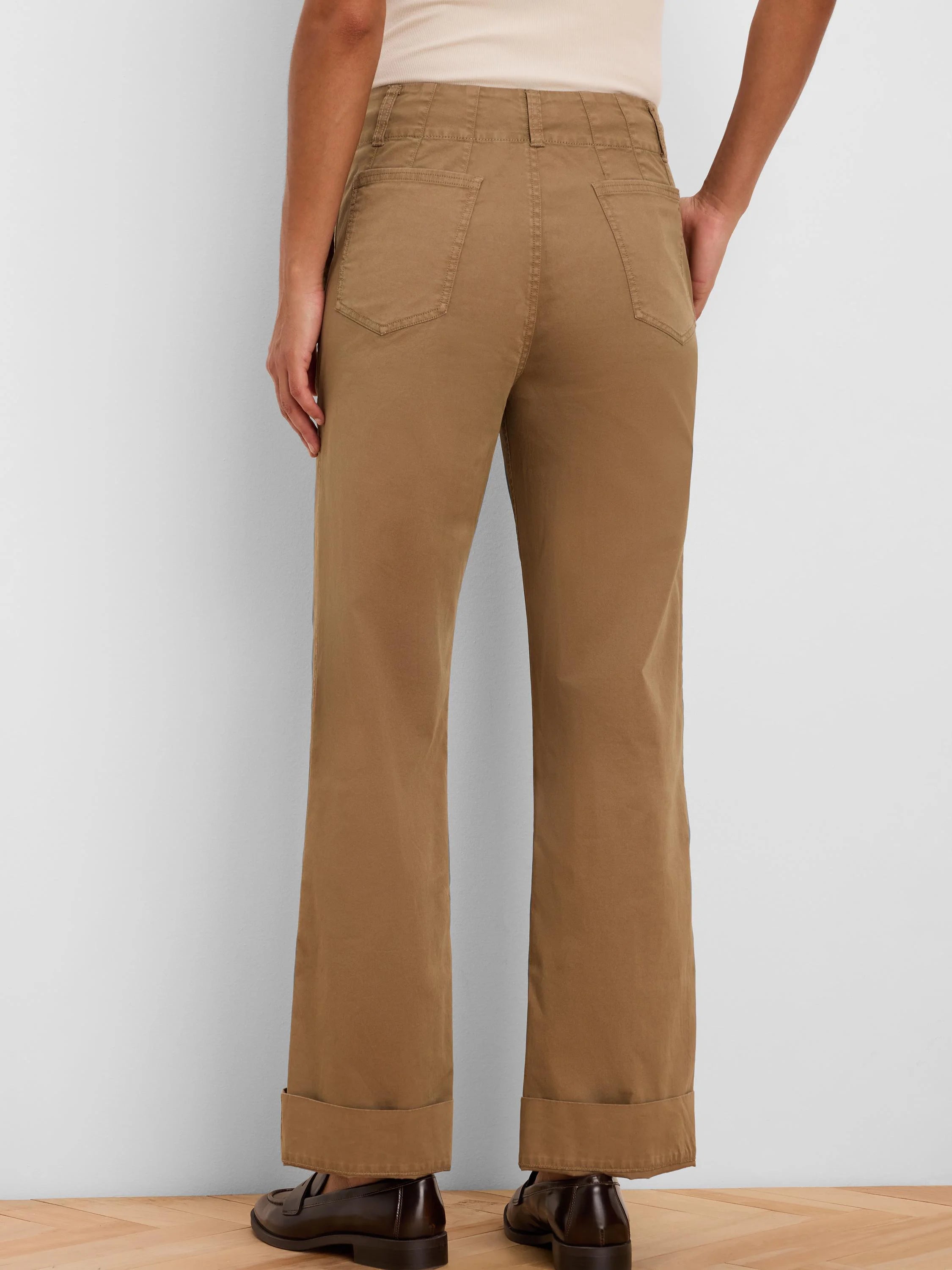 Tan high-waisted straight-leg pants, seen from behind, with patch back pockets and cuffed hems.