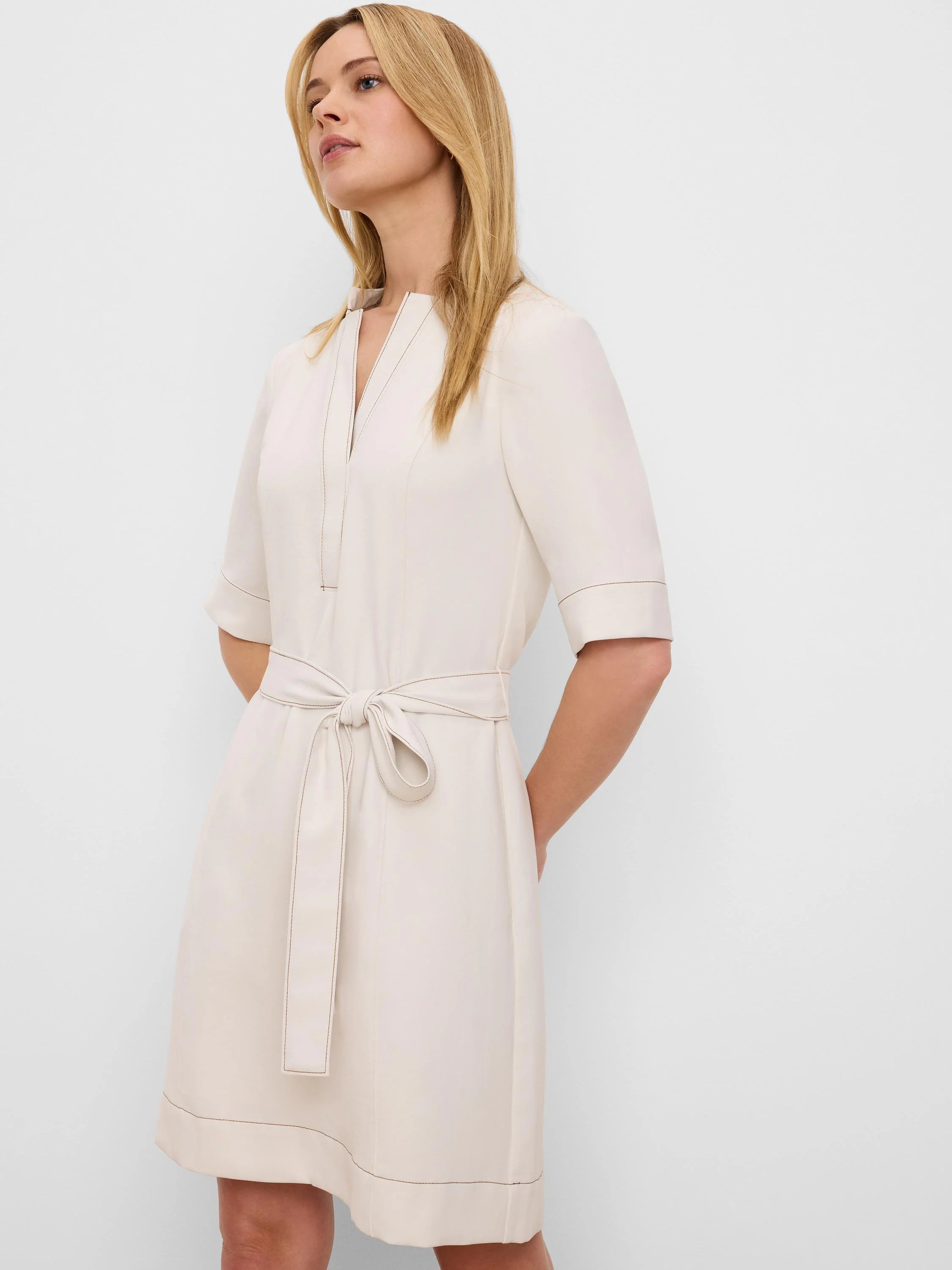 Beige V-neck dress with elbow sleeves, self-tie belt, and dark contrasting stitching, above-knee length.