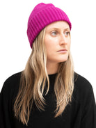 Magenta ribbed beanie hat with a flat crown, worn by a woman with blonde hair.