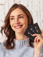 Woman holding three black cards with 'NIC ZOE' branding against a light background