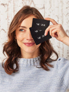 Woman holding black cards with 'Nic ZOE' branding in front of her eyes.