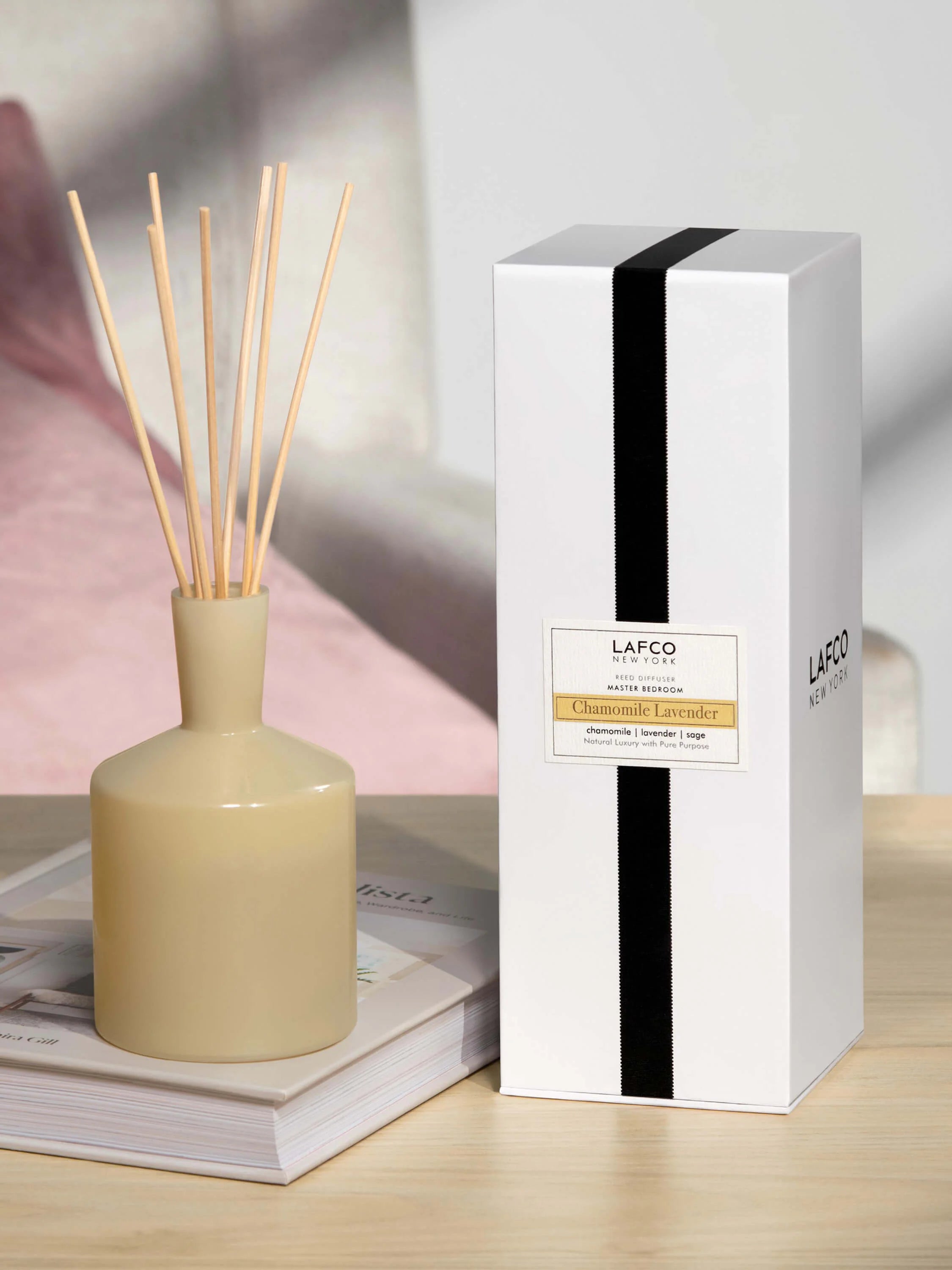 Round pale yellow diffuser bottle with light brown reeds. White product box features a black vertical stripe and yellow...