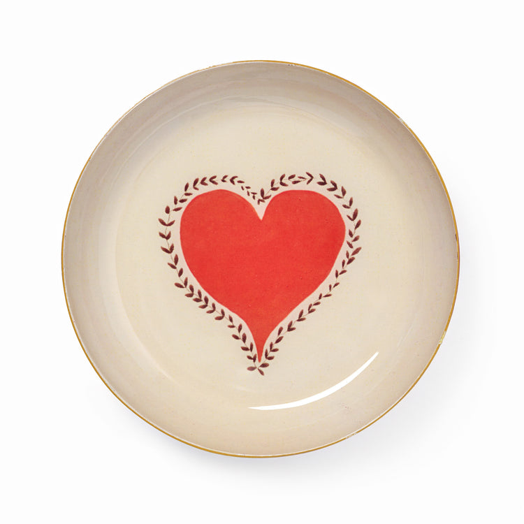 Cream ceramic dish with a red heart graphic centered within a dark vine pattern and accented by a golden yellow rim.