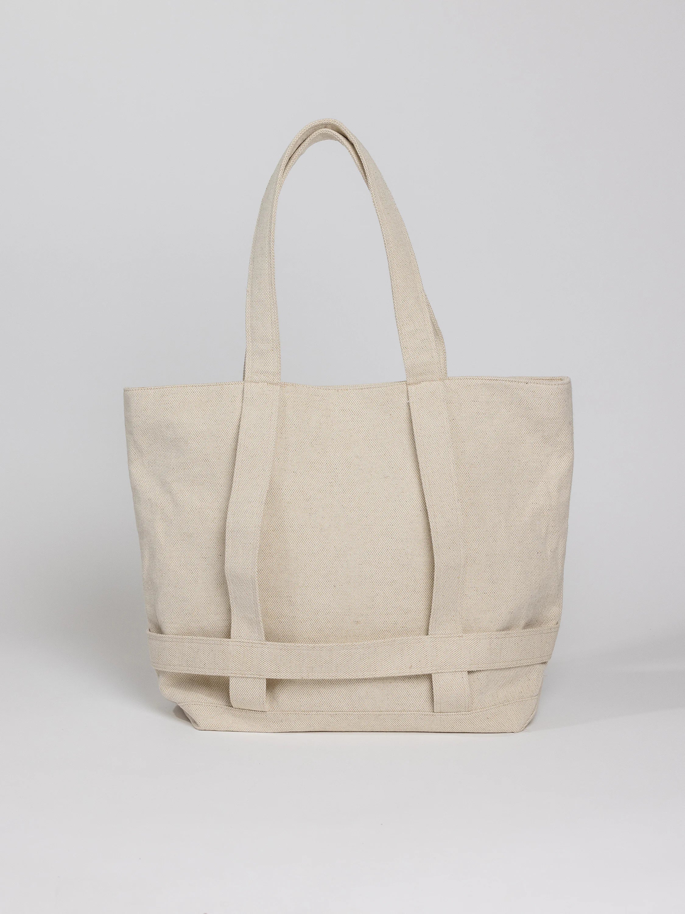Off-white canvas tote bag with two top handles and a reinforced bottom.  The bag features a woven detail across the bottom.