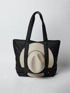 Black quilted tote bag with beige hat inside.  Bag has black straps.