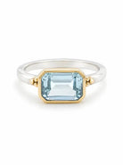 Silver ring with gold bezel-set emerald-cut light blue stone, flanked by small gold beads.
