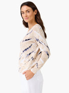Beige V-neck sweater with white and indigo blue brushstroke pattern. Long sleeves, ribbed cuffs.
