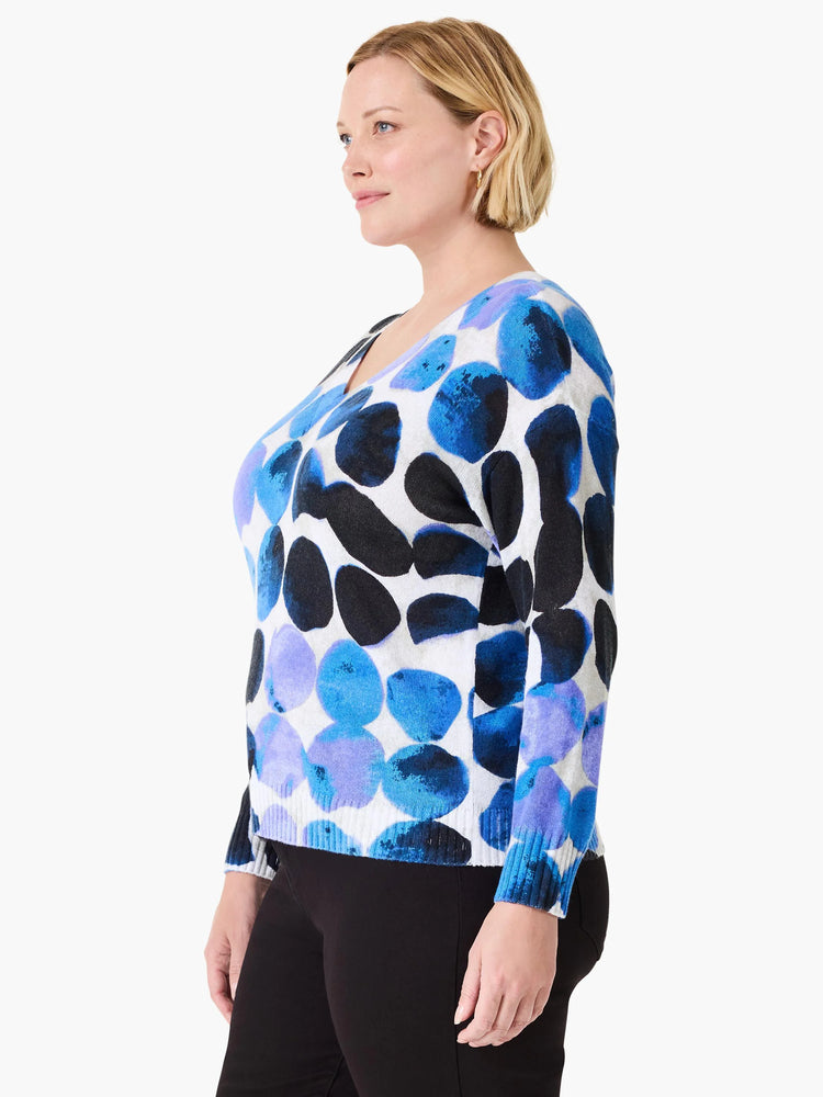 White V-neck sweater with large, irregular blue, purple, and black dots. Long sleeves.