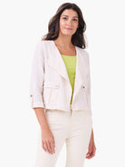 Pale beige linen moto jacket with draped lapel collar, chest snap pockets, and cuffed sleeves with snap tabs.