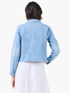 Light blue denim jacket, back view. Features a fringed hemline and vertical back seams.