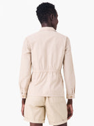 Back view of a light beige poplin jacket with long sleeves and a cinched elastic waist.