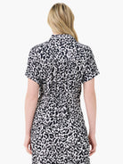 Back view of a woman in a monochrome animal print short-sleeve collared top with a gathered waist.