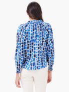White long-sleeve top with varied blue brushstroke pattern. Gathered neck & smocked cuffs. Model's back view.