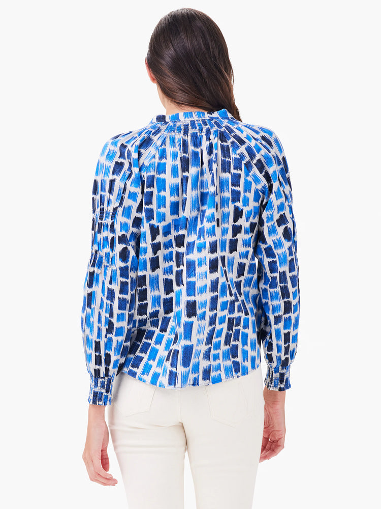 Long-sleeved blue & white top with abstract brushstroke pattern. Features a gathered high neck and smocked cuffs, viewed...