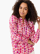 White top with pink & magenta brushstroke pattern. Long sleeves, smocked cuffs, and a V-neck mandarin collar.