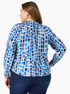 Woman in a white top with varied blue brushstroke rectangles, a gathered neckline, and smocked cuffs.