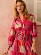 Sunset plaid shirt with pink, red, orange, and cream blocks. Features a V-neck, 3/4 elastic sleeves, and smocked waist.