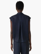 Back view of navy blue sleeveless collared top with rolled cap sleeves and a center back pleat.