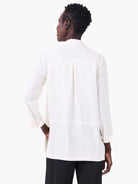 Off-white crepe shirt, loose, with long sleeves and rolled cuffs. Features a central pleat on the back.