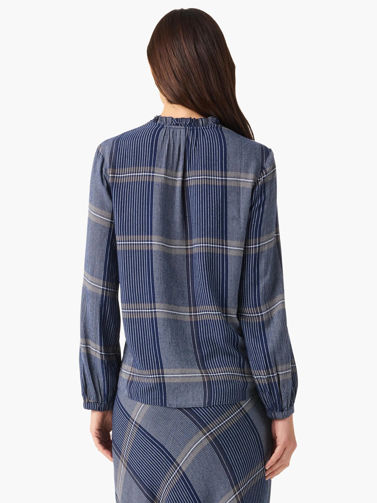Rear view of navy blue and taupe plaid long-sleeve blouse with ruffled neckline.  The blouse is shown paired with a...