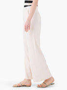 Off-white wide-leg linen trousers shown on a model.  The trousers are a creamy off-white color.