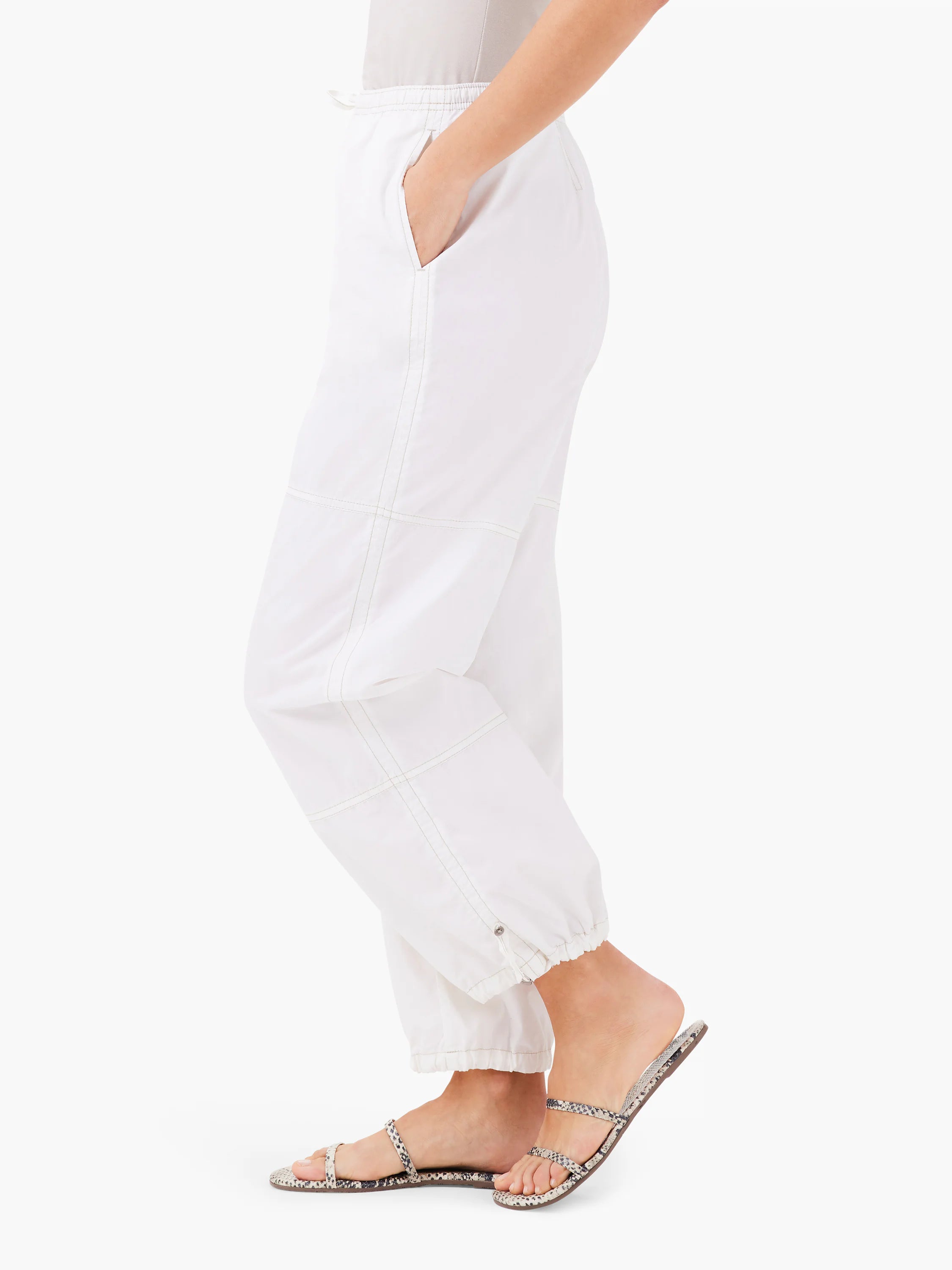 Off-white ankle pants with light beige stitching detail, elasticized cuffs, and side pockets.  Model wears sandals.