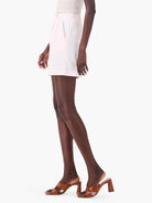 Off-white linen shorts, pleated front, pockets.  Model wears brown heels.