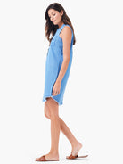 Light blue denim sleeveless mini dress, raw hem. Model shown wearing brown sandals.