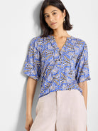 Blue top with a V-neck and short sleeves. Features a repeating geometric pattern in off-white and black.