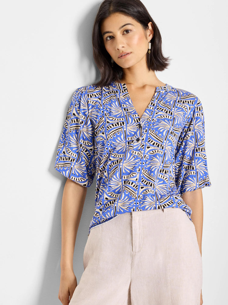 Blue top with a V-neck and short sleeves. Features a repeating geometric pattern in off-white and black.