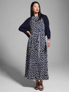 Navy blue shrug cardigan over a midi dress with a white and navy abstract print.  Dress has a self-tie belt.