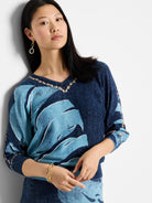 V-neck sweater; navy blue and light blue abstract leaf pattern;  brown and gold neckline detail. Three-quarter sleeves.