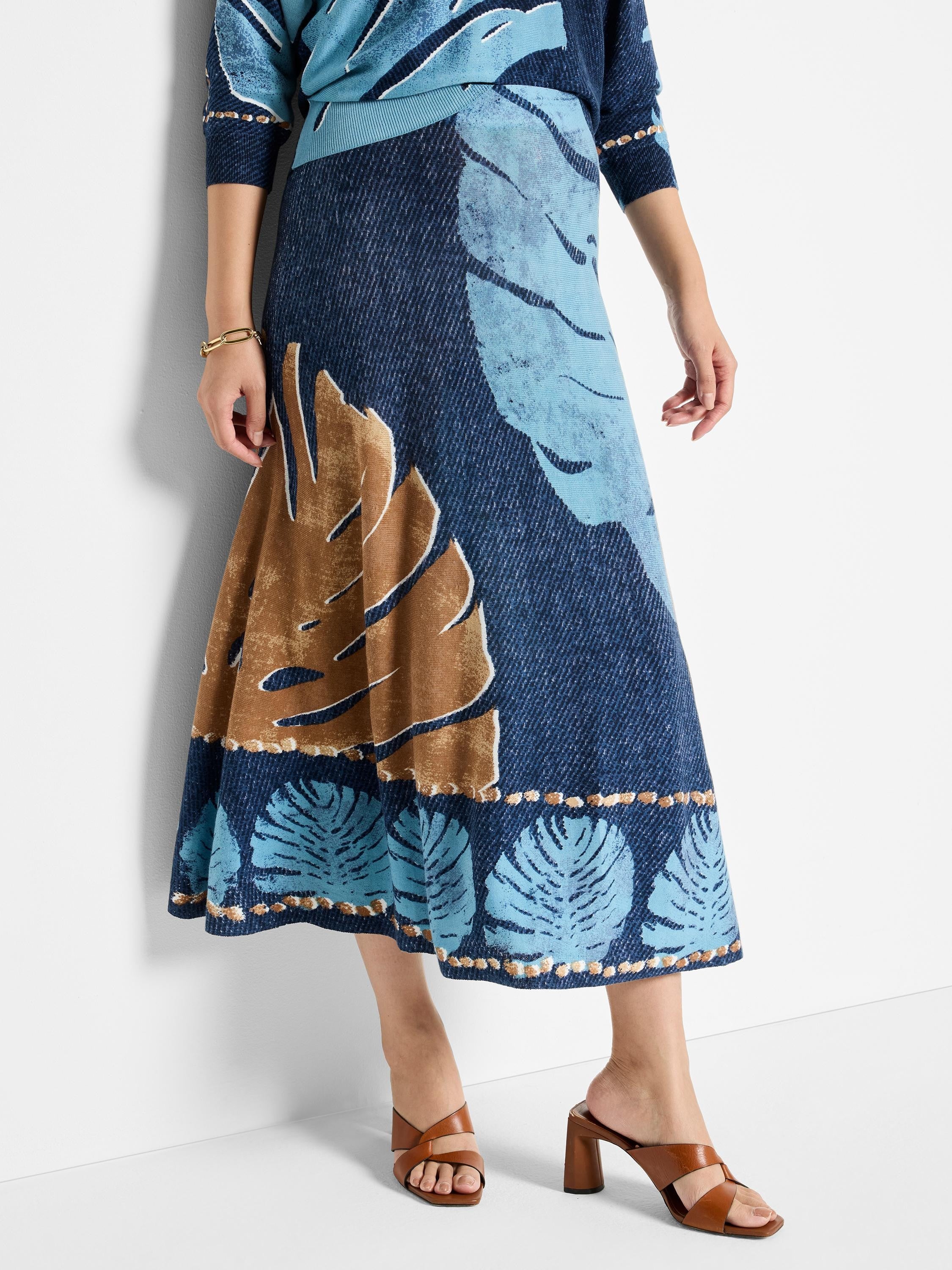 Knit midi skirt in blue, light blue, and brown. Features a leaf print and a textured hemline.