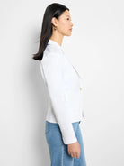 White blazer, side view.  Features two pockets and gold buttons.  The blazer has long sleeves with buttoned cuffs.