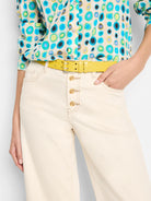 Yellow belt with textured surface; off-white pants; shirt with teal, blue, green circles on beige background.