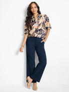 Beige top with dark blue/black leaf print, short sleeves.  Model wears navy blue wide-leg trousers and nude heels.