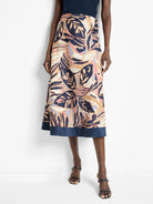 Midi-length terracotta skirt with a dark navy blue bottom band. Features a leaf print in shades of beige, dark blue, and...