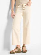 Off-white wide-leg jeans with gold buttons.  Jeans have a slight cuff. Model wears olive green sandals.