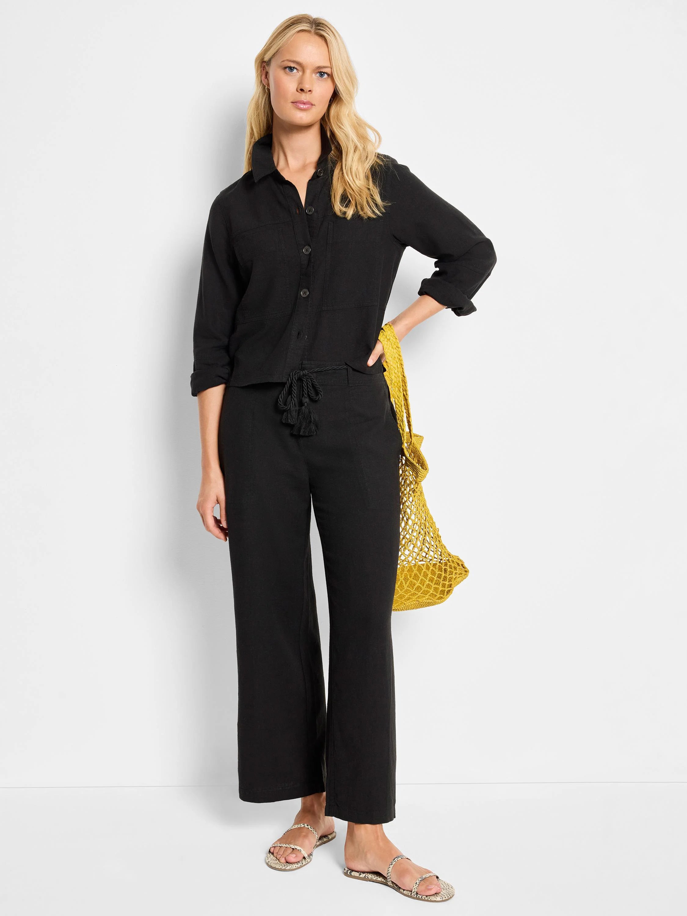 Black wide-leg linen pants with drawstring waist and black tassels.  Model also wears black shirt and light-colored sandals.