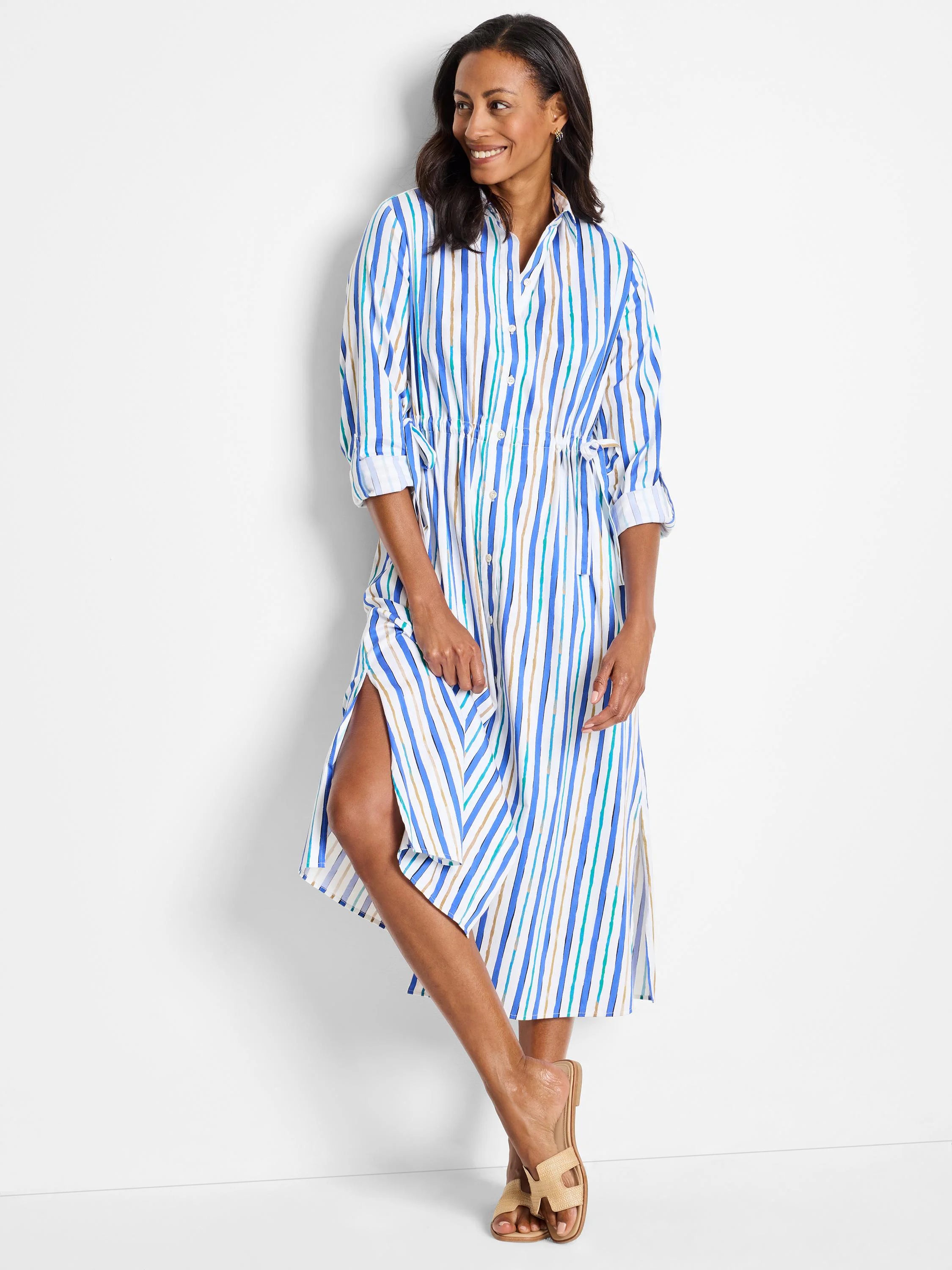 White midi dress with blue, teal, and beige vertical stripes.  Shirt style, long sleeves, side slits, and cinched waist.