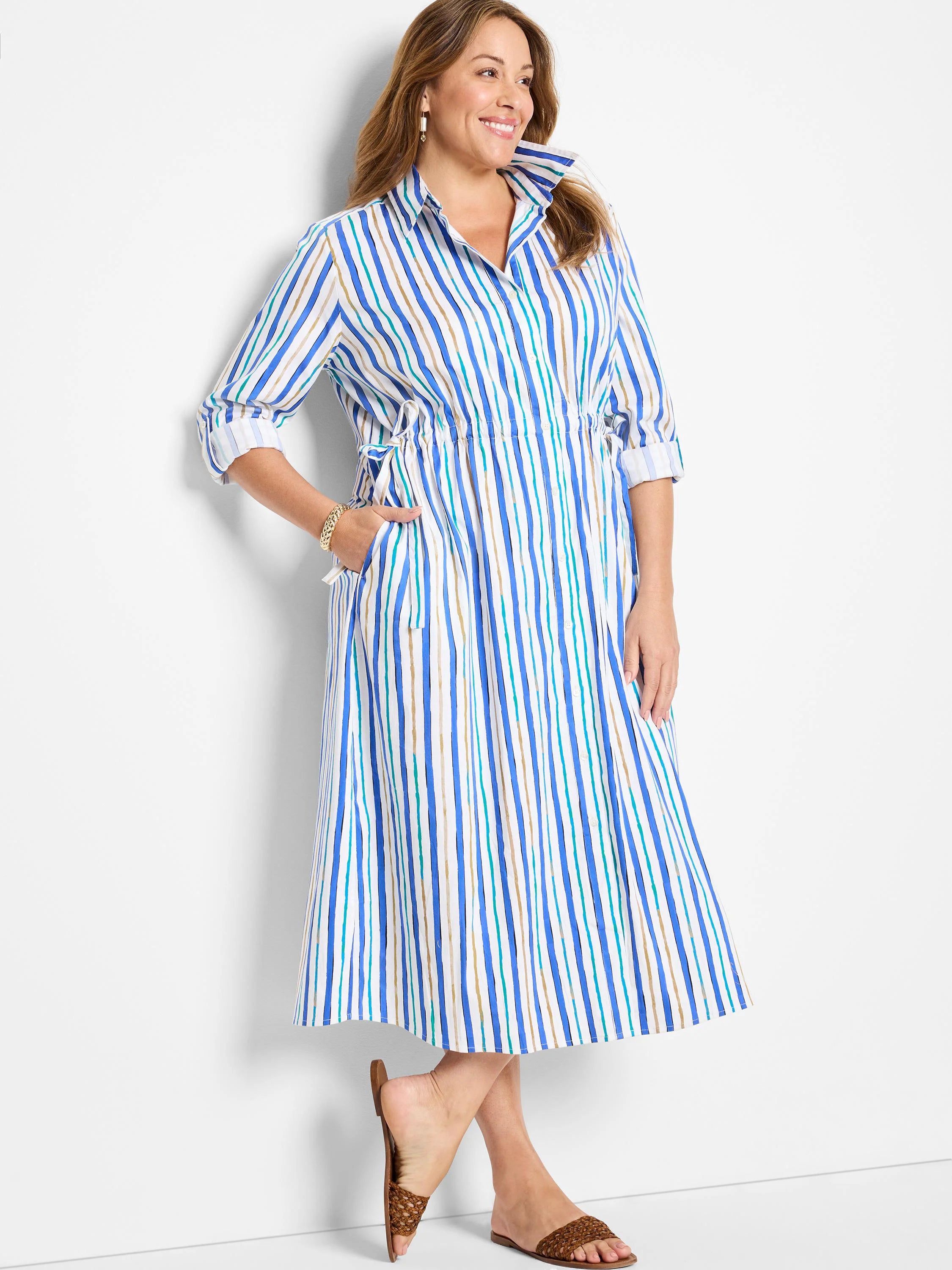 White midi dress with vertical blue, teal, and gold stripes.  Long sleeves, button front, and cinched waist.
