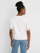 White top with elbow-length sleeves featuring decorative cut-out edges.