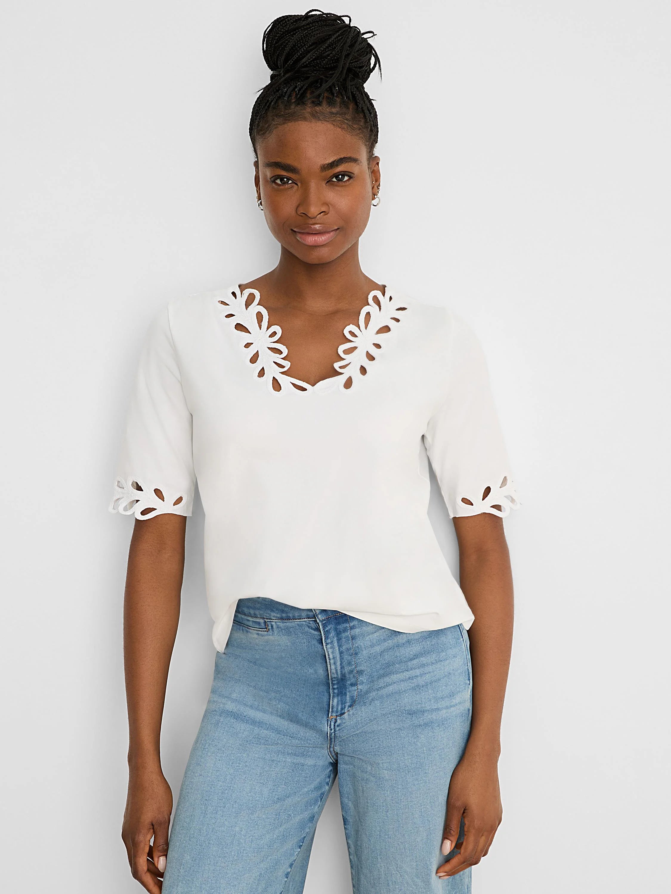 White V-neck top with short sleeves. Floral cutout edges on the neckline and sleeve cuffs.