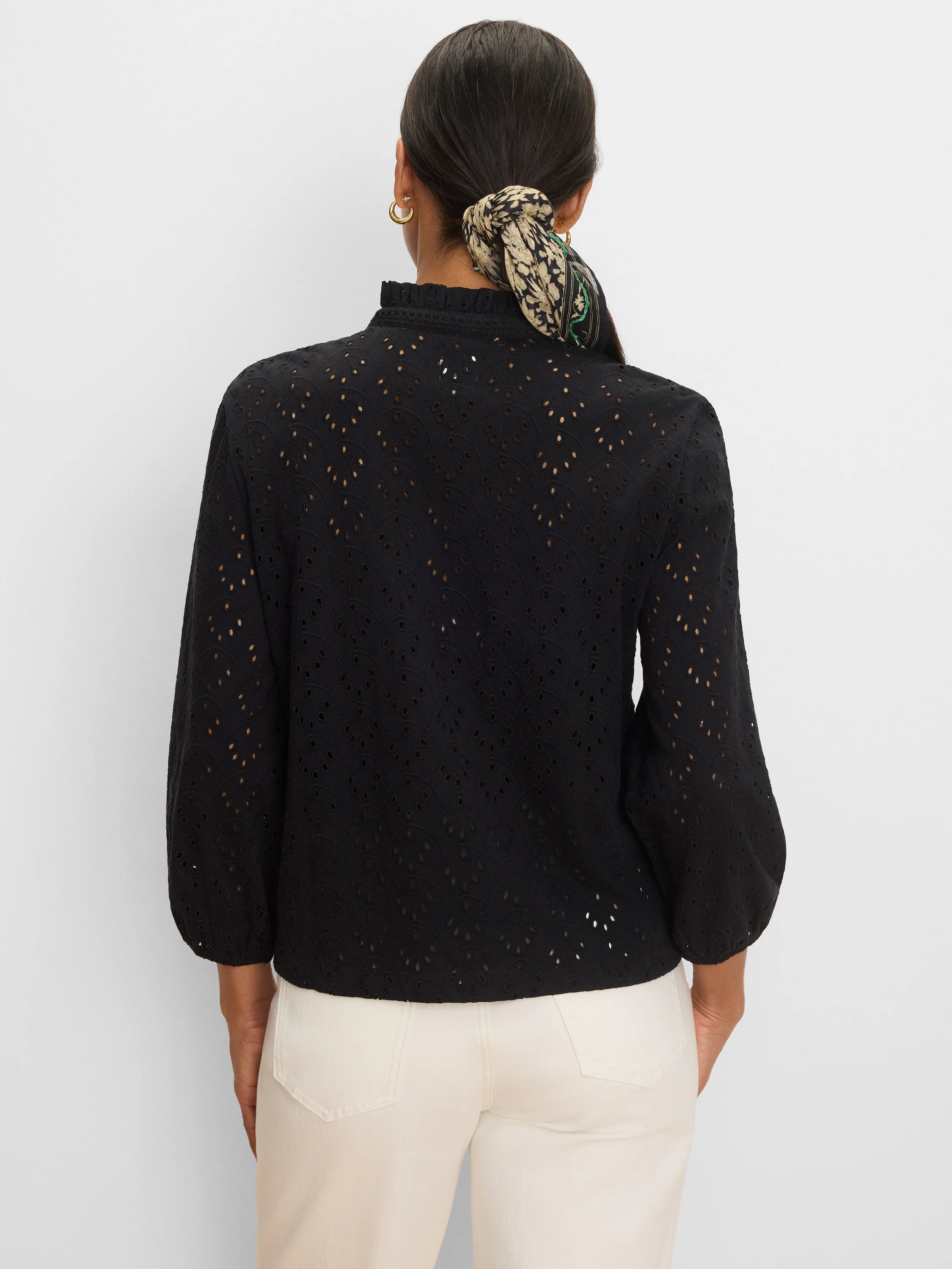 Black knit top with a ruffled high neck, long voluminous sleeves, and an all-over scalloped eyelet pattern.